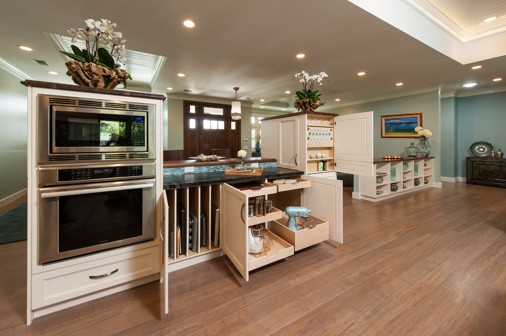 Large transitional l-shaped bamboo floor open concept kitchen photo in Hawaii with an undermount sink, shaker cabinets, white cabinets, soapstone countertops, blue backsplash, glass sheet backsplash, paneled appliances and an island