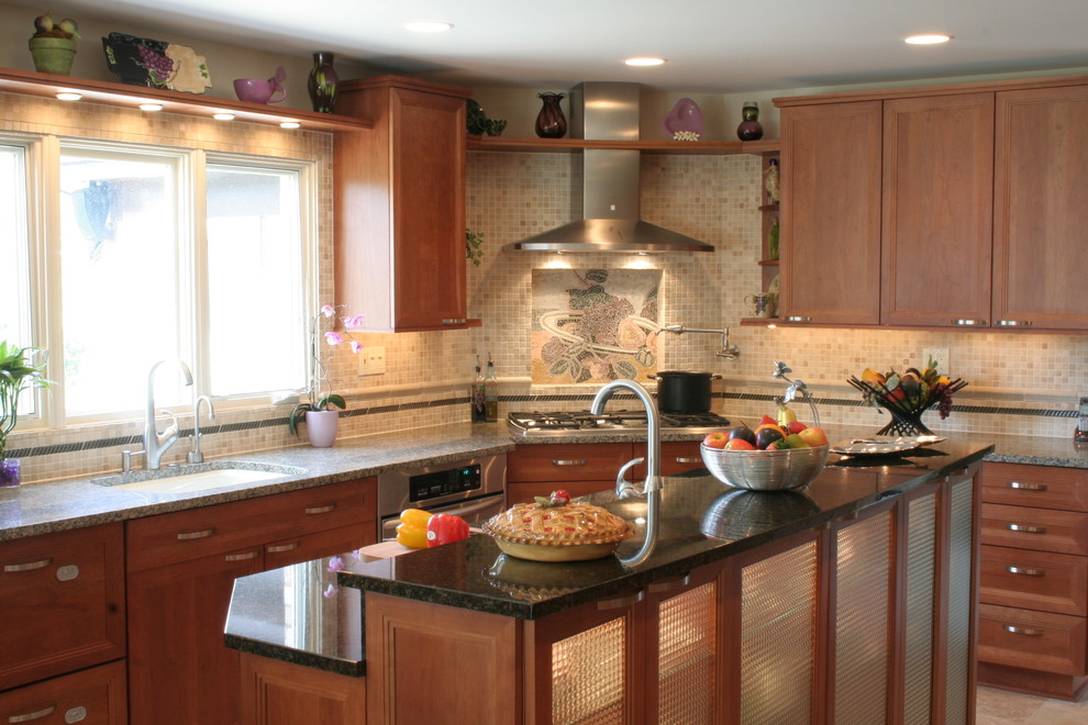Cette photo montre une cuisine américaine chic en U et bois clair avec un évier encastré, un placard à porte plane, un plan de travail en granite, une crédence beige et un électroménager en acier inoxydable.