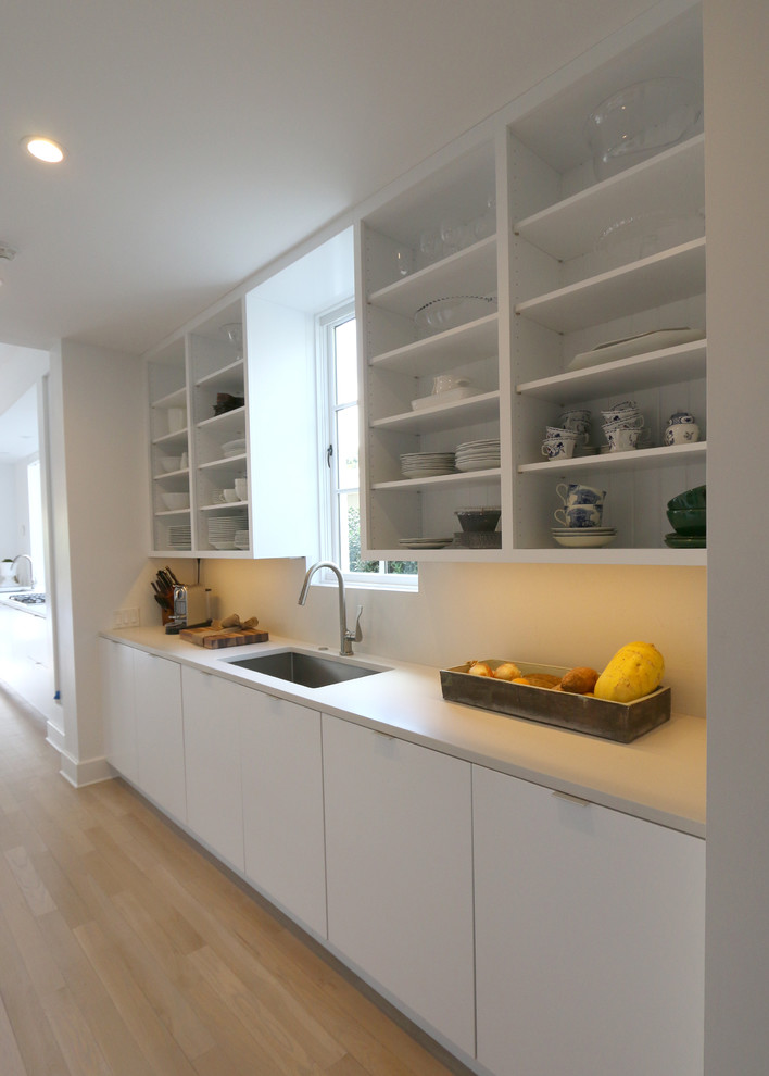Idéer för att renovera ett stort funkis vit vitt u-kök, med en undermonterad diskho, släta luckor, vita skåp, marmorbänkskiva, vitt stänkskydd, rostfria vitvaror, ljust trägolv och en köksö