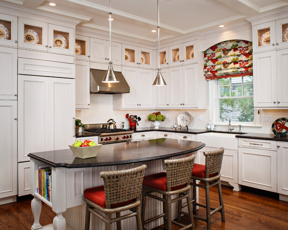 Klassische Küche in L-Form mit Landhausspüle, Kassettenfronten, weißen Schränken, Küchenrückwand in Weiß, braunem Holzboden, Kücheninsel und Elektrogeräten mit Frontblende in New York