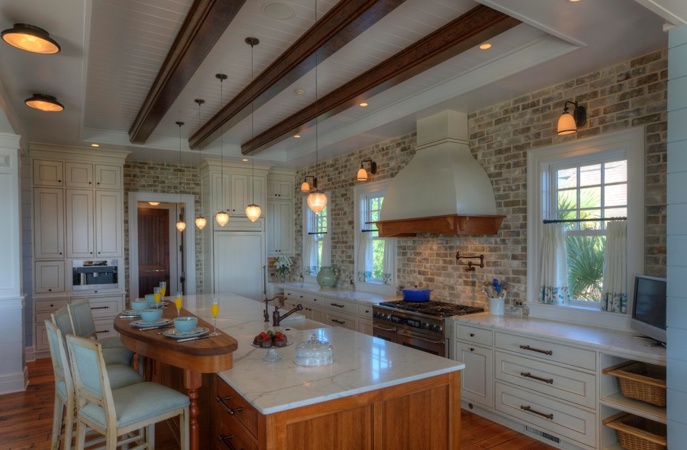 Foto på ett vit kök, med marmorbänkskiva, en enkel diskho, vita skåp, stänkskydd i tegel, rostfria vitvaror, en köksö och brunt golv