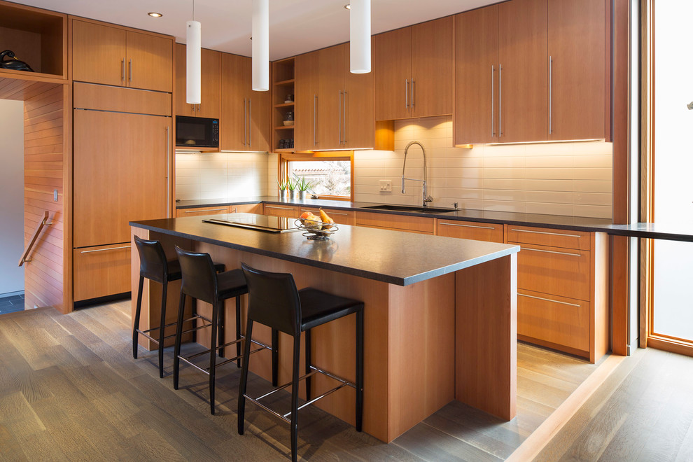 Moderne Küche in L-Form mit flächenbündigen Schrankfronten, hellbraunen Holzschränken, Küchenrückwand in Weiß, Elektrogeräten mit Frontblende, braunem Holzboden und Kücheninsel in Minneapolis