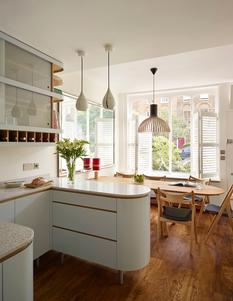 Mid-sized trendy medium tone wood floor eat-in kitchen photo in London with a single-bowl sink, flat-panel cabinets, gray cabinets, solid surface countertops, white backsplash, glass sheet backsplash, stainless steel appliances and no island