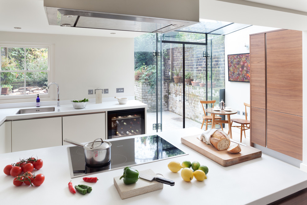 Moderne Wohnküche in U-Form mit Unterbauwaschbecken, weißen Schränken, Mineralwerkstoff-Arbeitsplatte, Elektrogeräten mit Frontblende und flächenbündigen Schrankfronten in London