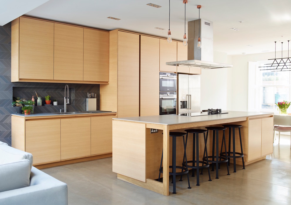 Photo of a contemporary galley open plan kitchen in London with a built-in sink, flat-panel cabinets, light wood cabinets, black splashback, stainless steel appliances, concrete flooring, an island and grey floors.