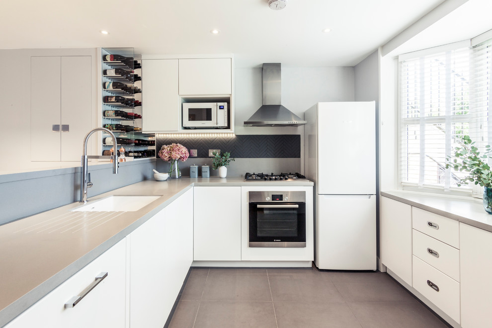 Immagine di una cucina a L chic con lavello sottopiano, ante lisce, ante bianche, paraspruzzi nero, elettrodomestici in acciaio inossidabile e pavimento grigio