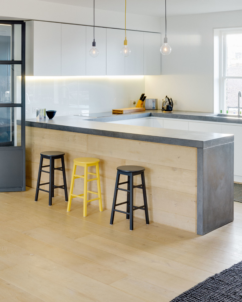 Modelo de cocinas en U actual con armarios con paneles lisos, puertas de armario blancas, encimera de cemento, suelo de madera clara, península y suelo beige
