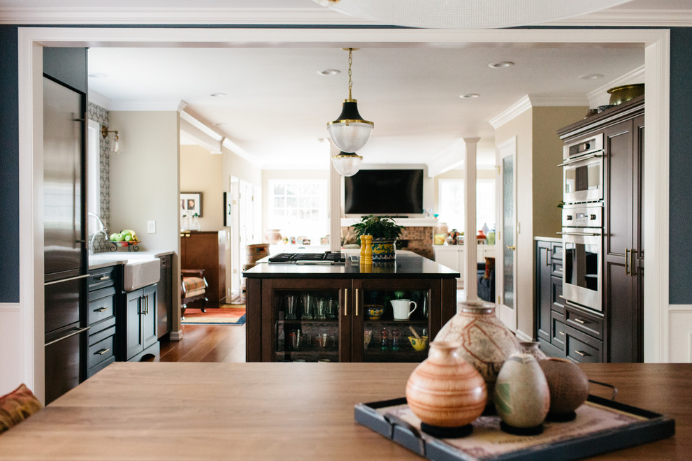 Eat-in kitchen - mid-sized medium tone wood floor and red floor eat-in kitchen idea in Seattle with a farmhouse sink, recessed-panel cabinets, brown cabinets, quartzite countertops, gray backsplash, porcelain backsplash, stainless steel appliances, an island and black countertops