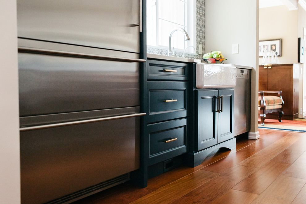 Klassisk inredning av ett mellanstort vit vitt kök och matrum, med en rustik diskho, luckor med infälld panel, blå skåp, bänkskiva i kvarts, grått stänkskydd, stänkskydd i porslinskakel, rostfria vitvaror, mellanmörkt trägolv, en köksö och rött golv