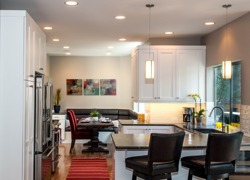 Example of a mid-sized transitional l-shaped medium tone wood floor eat-in kitchen design in Seattle with an undermount sink, shaker cabinets, white cabinets, limestone countertops, white backsplash, subway tile backsplash, stainless steel appliances and no island