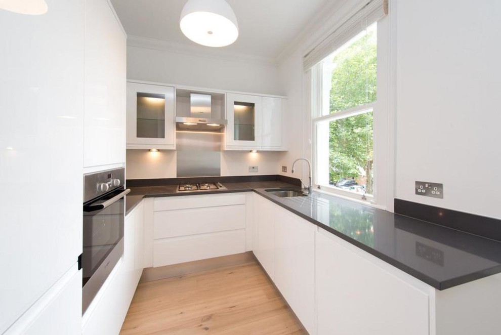 Inspiration for a small modern u-shaped enclosed kitchen in London with a single-bowl sink, flat-panel cabinets, white cabinets, granite worktops, metallic splashback, metal splashback, stainless steel appliances and light hardwood flooring.