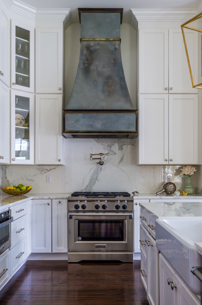 Kitchen - mid-sized transitional u-shaped dark wood floor and brown floor kitchen idea in New Orleans with a farmhouse sink, recessed-panel cabinets, white cabinets, marble countertops, white backsplash, stone slab backsplash, stainless steel appliances and an island
