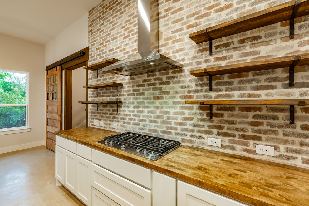 Idéer för stora lantliga brunt kök, med en undermonterad diskho, luckor med infälld panel, vita skåp, träbänkskiva, rött stänkskydd, stänkskydd i tegel, rostfria vitvaror, betonggolv, en köksö och grått golv