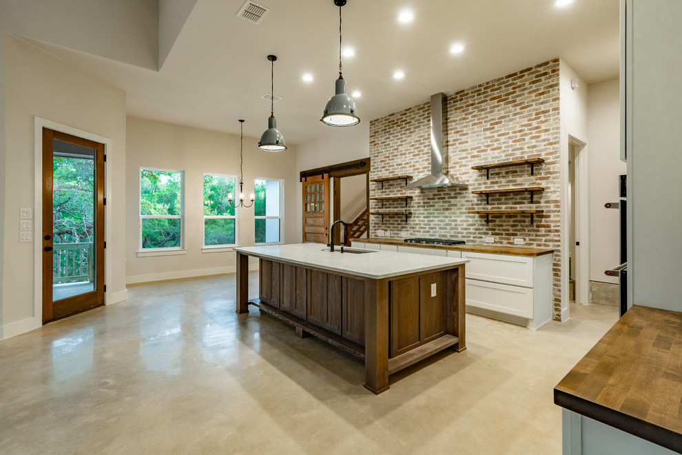 Example of a large cottage u-shaped concrete floor and gray floor eat-in kitchen design in Austin with an undermount sink, recessed-panel cabinets, white cabinets, wood countertops, red backsplash, brick backsplash, stainless steel appliances, an island and brown countertops