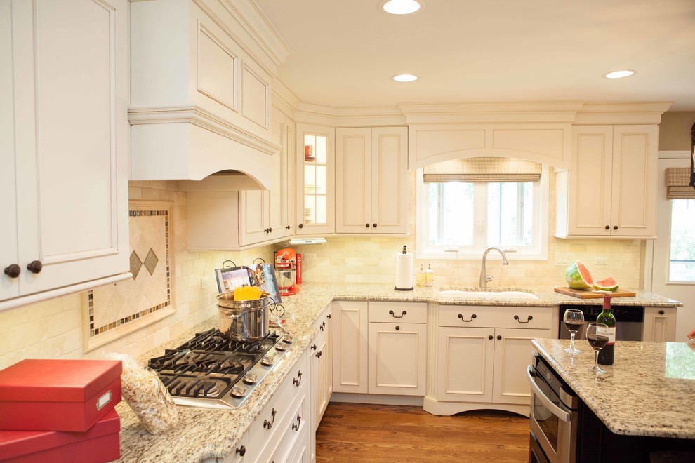Example of a large trendy u-shaped medium tone wood floor eat-in kitchen design in Chicago with an undermount sink, recessed-panel cabinets, white cabinets, granite countertops, beige backsplash, stone slab backsplash, stainless steel appliances and an island