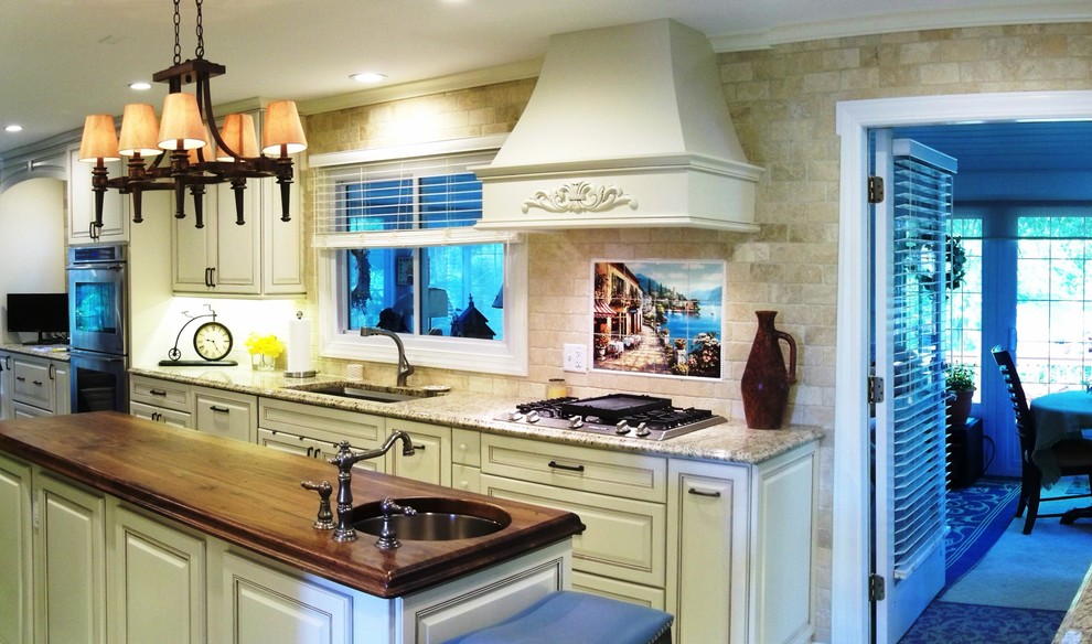 Example of a huge tuscan galley porcelain tile eat-in kitchen design in Baltimore with an undermount sink, raised-panel cabinets, beige cabinets, granite countertops, beige backsplash, stone tile backsplash, stainless steel appliances and an island
