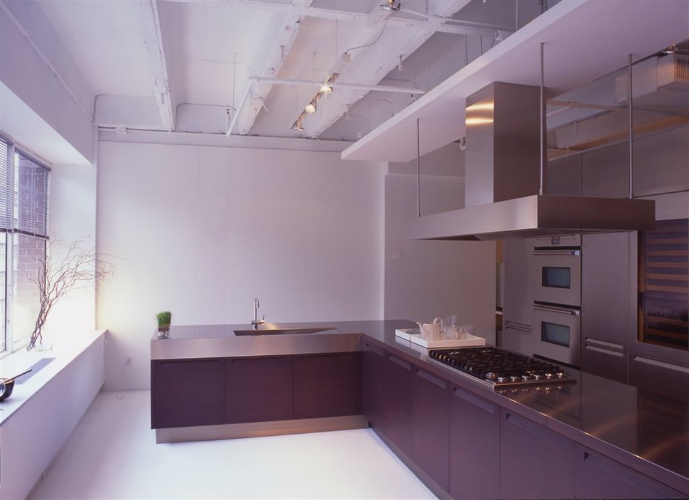 Large modern l-shaped kitchen pantry in New York with a breakfast bar, flat-panel cabinets, stainless steel cabinets, stainless steel worktops, stainless steel appliances, a submerged sink and light hardwood flooring.