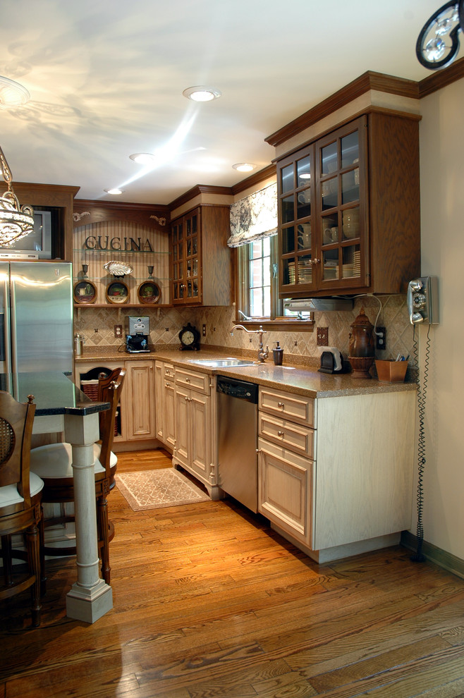 Example of a mid-sized tuscan u-shaped medium tone wood floor eat-in kitchen design in Indianapolis with an undermount sink, raised-panel cabinets, beige cabinets, stainless steel appliances, an island, granite countertops, beige backsplash and stone tile backsplash