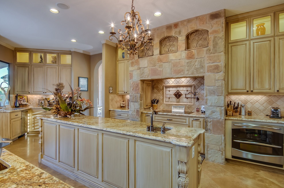 Kitchen pantry - large transitional single-wall ceramic tile kitchen pantry idea in Austin with an undermount sink, raised-panel cabinets, light wood cabinets, granite countertops, beige backsplash, stone tile backsplash, stainless steel appliances and an island