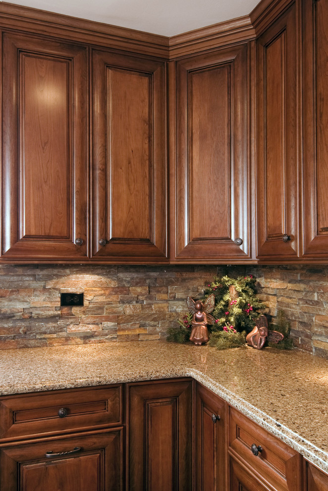 Exempel på ett avskilt, mellanstort klassiskt l-kök, med luckor med upphöjd panel, skåp i mellenmörkt trä, granitbänkskiva, brunt stänkskydd, stänkskydd i stenkakel, integrerade vitvaror, mörkt trägolv, en köksö och brunt golv