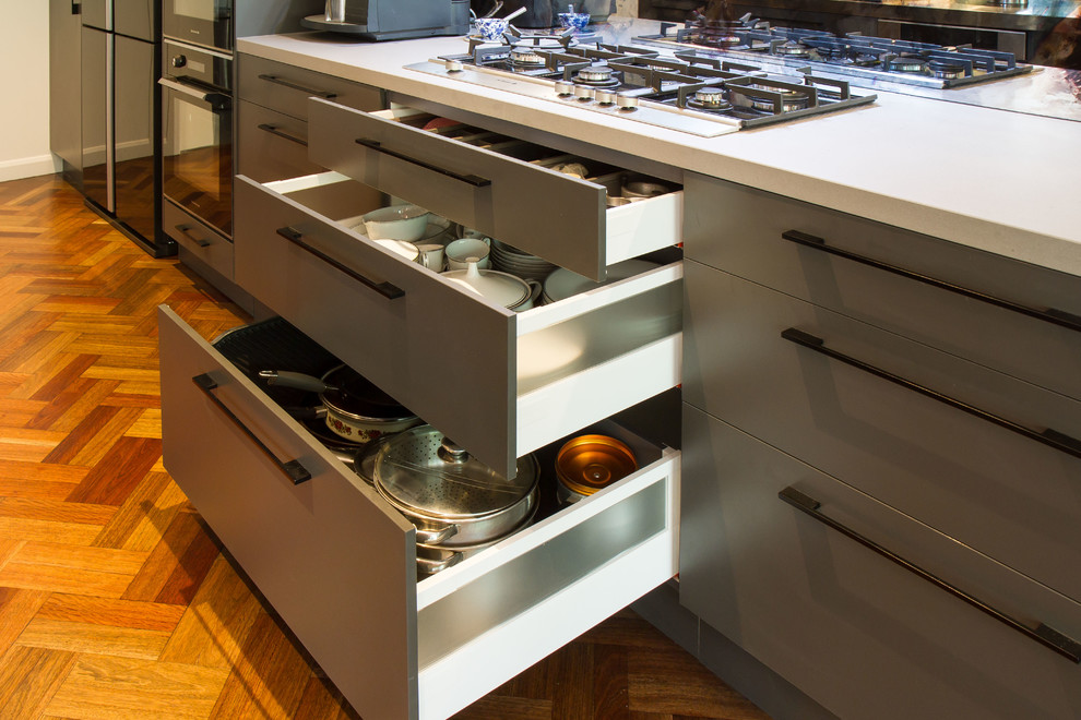 Idéer för ett mellanstort modernt kök, med släta luckor, grå skåp, bänkskiva i rostfritt stål, spegel som stänkskydd, svarta vitvaror, mellanmörkt trägolv och en köksö