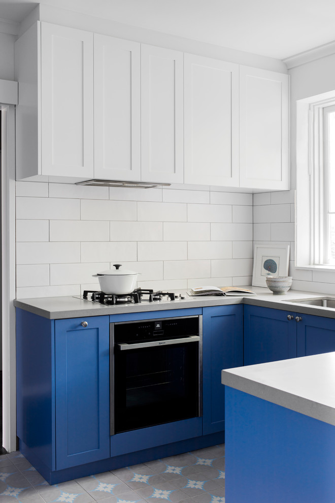 Photo of a small contemporary u-shaped enclosed kitchen in Melbourne with a submerged sink, shaker cabinets, blue cabinets, engineered stone countertops, white splashback, porcelain splashback, stainless steel appliances, concrete flooring, no island and multi-coloured floors.