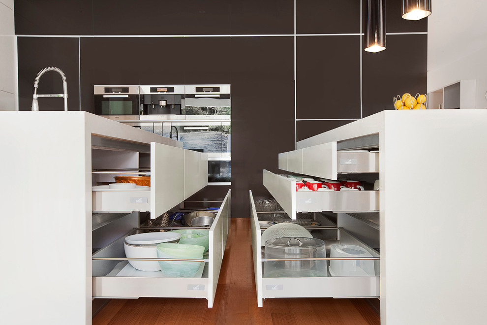 メルボルンにあるモダンスタイルのおしゃれなキッチン (アンダーカウンターシンク、クオーツストーンカウンター、白いキッチンパネル、ガラス板のキッチンパネル、黒い調理設備、淡色無垢フローリング) の写真