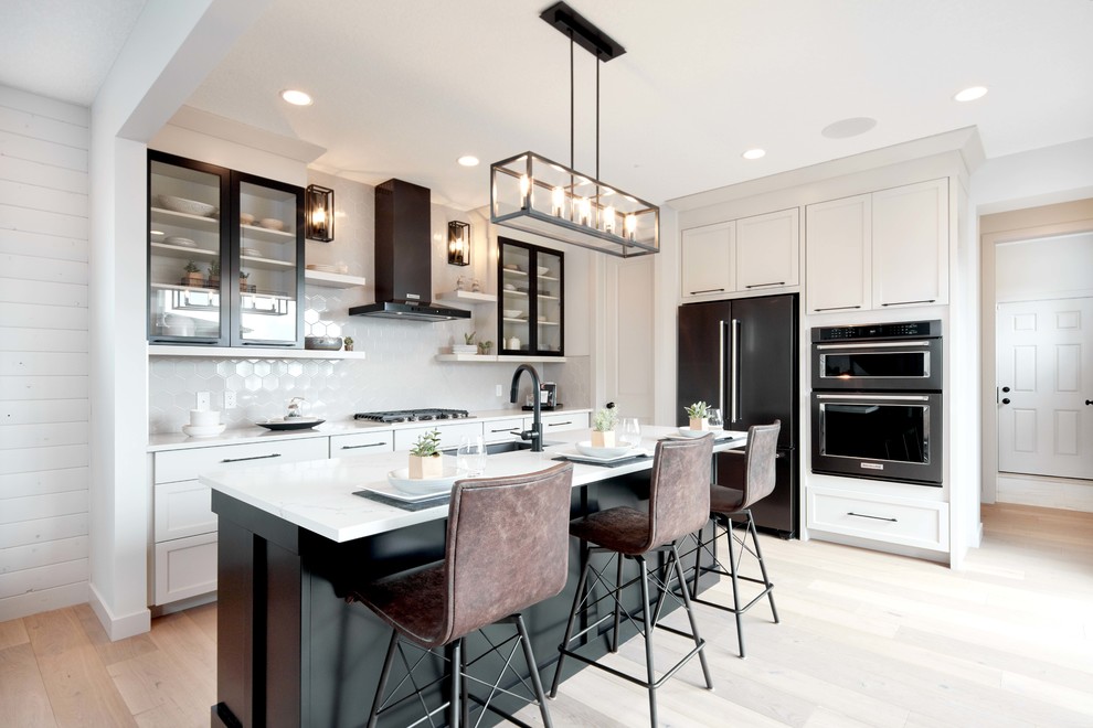 Design ideas for a traditional l-shaped kitchen/diner in Calgary with a submerged sink, recessed-panel cabinets, white cabinets, engineered stone countertops, white splashback, ceramic splashback, black appliances, an island, white worktops, light hardwood flooring and beige floors.