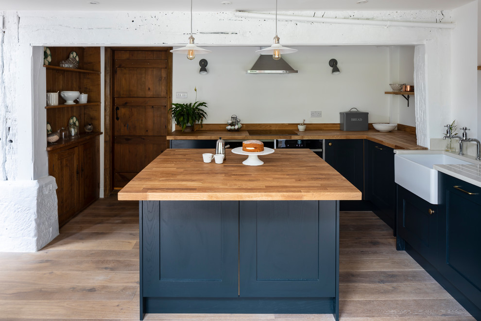 Inspiration for a medium sized farmhouse l-shaped kitchen in London with a belfast sink, recessed-panel cabinets, blue cabinets, wood worktops, stainless steel appliances, light hardwood flooring, an island, brown floors and beige worktops.