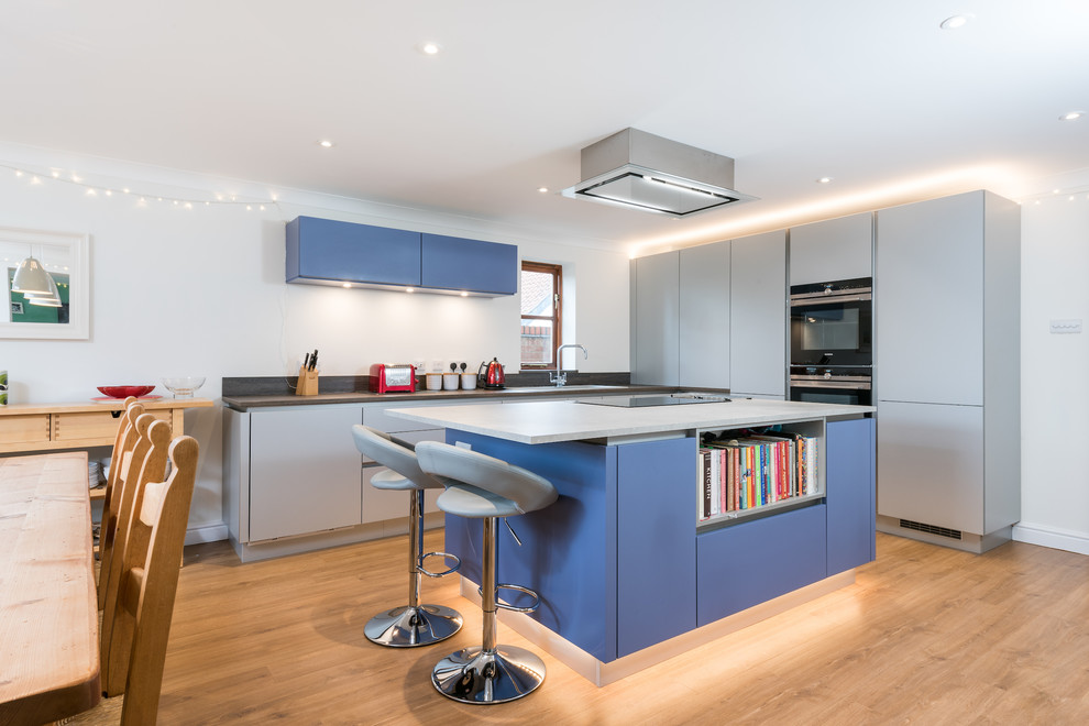 This is an example of a contemporary kitchen/diner in Other with flat-panel cabinets, blue cabinets, black appliances, light hardwood flooring, an island and grey worktops.