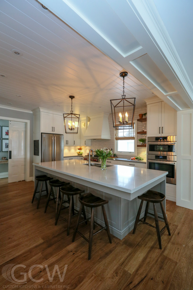 Foto på ett stort lantligt kök, med skåp i shakerstil, vita skåp, stänkskydd i keramik, rostfria vitvaror, mellanmörkt trägolv, en köksö och brunt golv