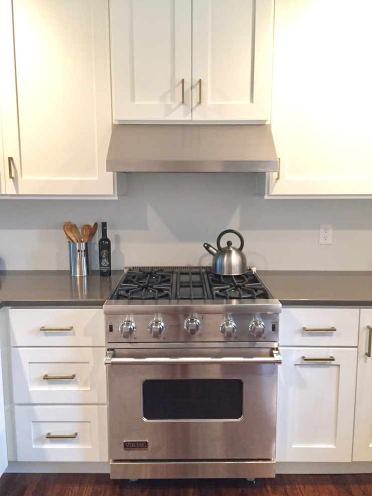 Inredning av ett amerikanskt litet grå grått kök, med en undermonterad diskho, skåp i shakerstil, vita skåp, bänkskiva i kvarts, rostfria vitvaror, mörkt trägolv, en halv köksö och brunt golv
