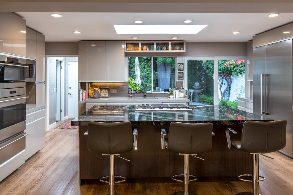 Inspiration for a large contemporary u-shaped medium tone wood floor open concept kitchen remodel in Los Angeles with an undermount sink, flat-panel cabinets, gray cabinets, quartz countertops, gray backsplash, glass tile backsplash, stainless steel appliances and an island