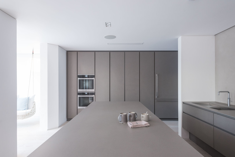 This is an example of a large contemporary kitchen in London with an integrated sink, flat-panel cabinets, grey cabinets, light hardwood flooring and an island.