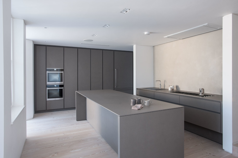 Large contemporary kitchen in London with an integrated sink, flat-panel cabinets, grey cabinets, light hardwood flooring and an island.