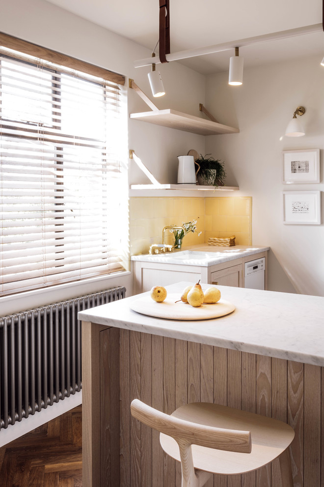 Cette image montre une cuisine rustique en bois clair avec plan de travail en marbre, îlot, un évier posé, un placard à porte shaker, une crédence beige, un électroménager blanc et un sol en bois brun.