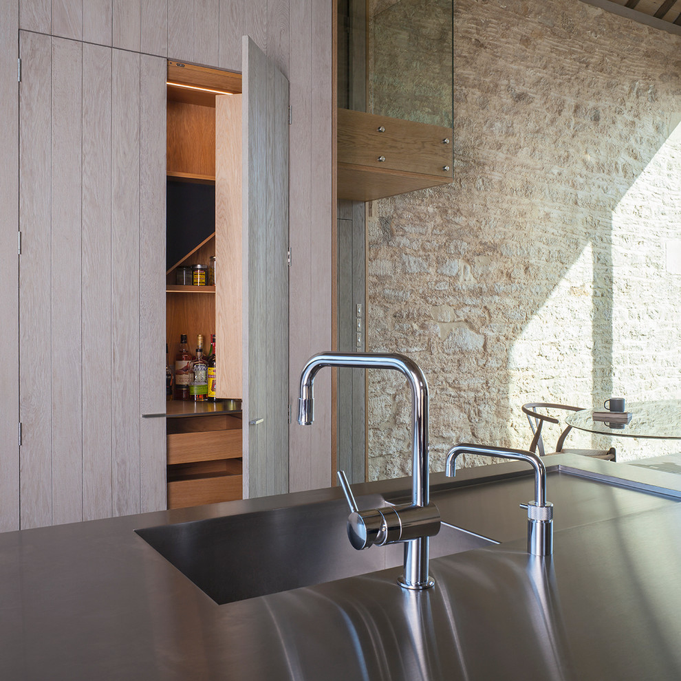 На фото: кухня-гостиная в стиле кантри с искусственно-состаренными фасадами, столешницей из нержавеющей стали и островом