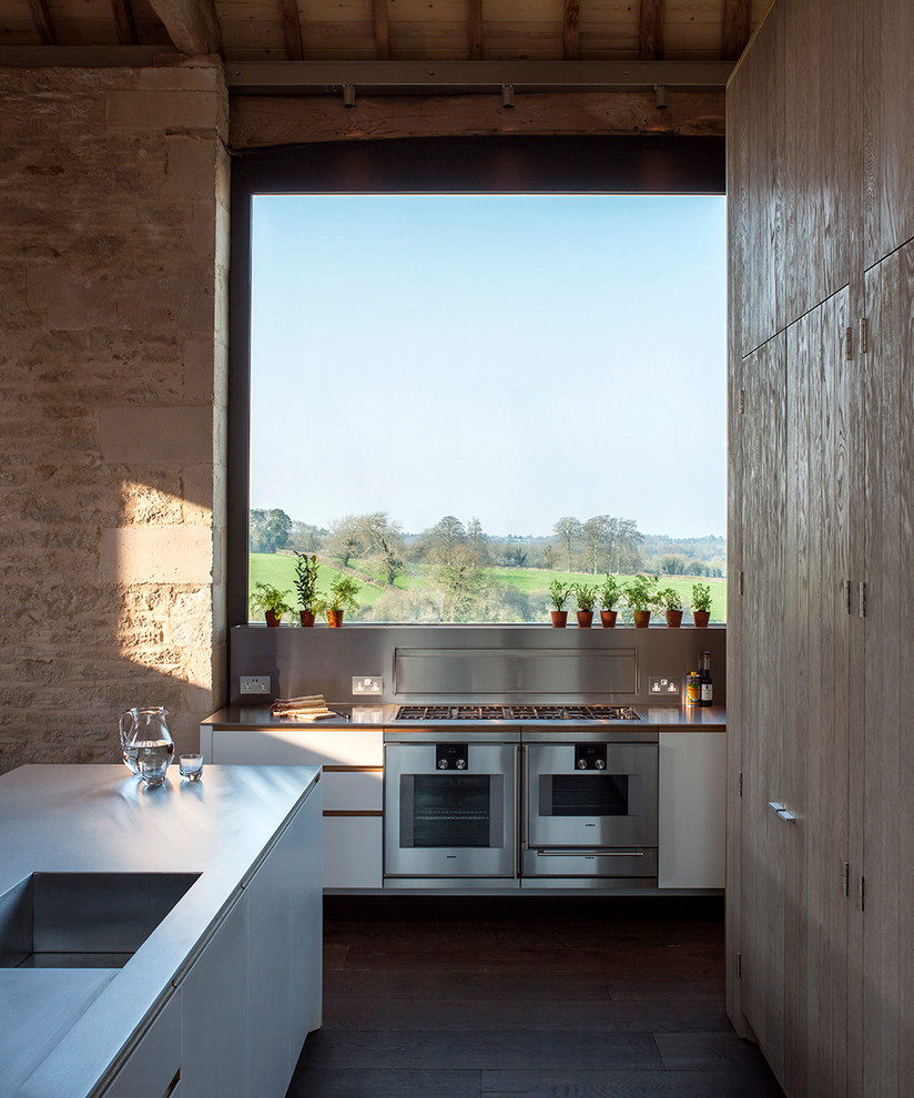 Imagen de cocina de estilo de casa de campo abierta con puertas de armario con efecto envejecido, encimera de acero inoxidable y una isla
