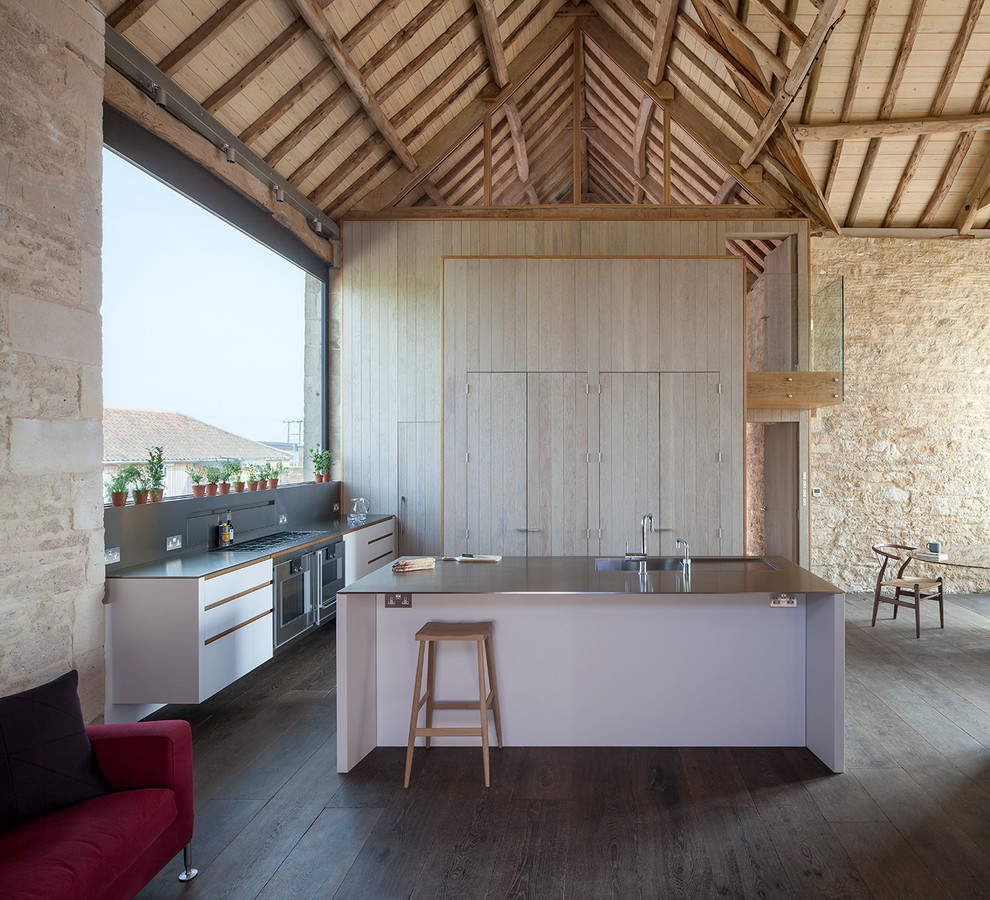 На фото: кухня-гостиная в стиле кантри с искусственно-состаренными фасадами, столешницей из нержавеющей стали и островом с