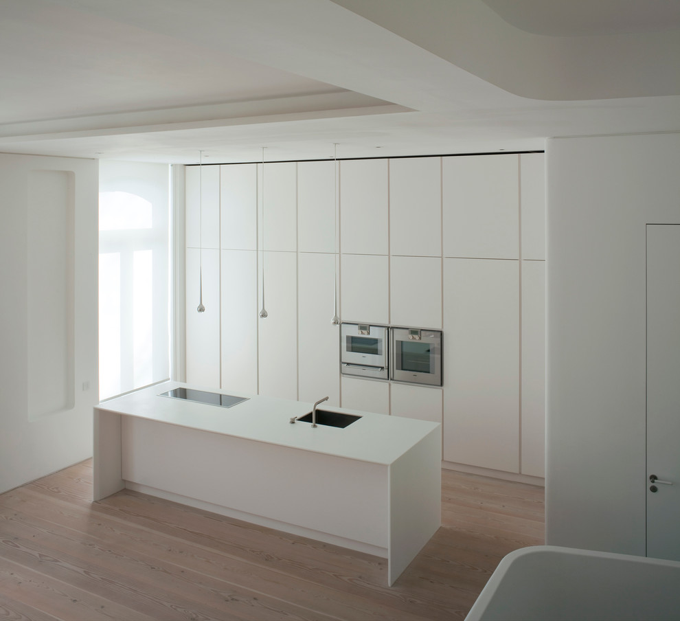 Cette image montre une cuisine linéaire design avec îlot, un placard à porte plane, des portes de placard blanches, un électroménager en acier inoxydable et parquet clair.