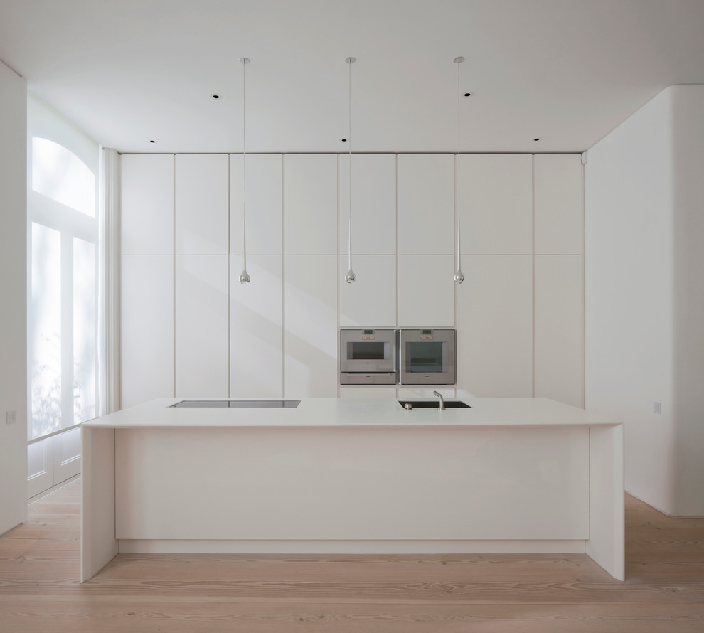 Inspiration for a contemporary single-wall kitchen in London with an island, flat-panel cabinets, white cabinets, stainless steel appliances and light hardwood flooring.