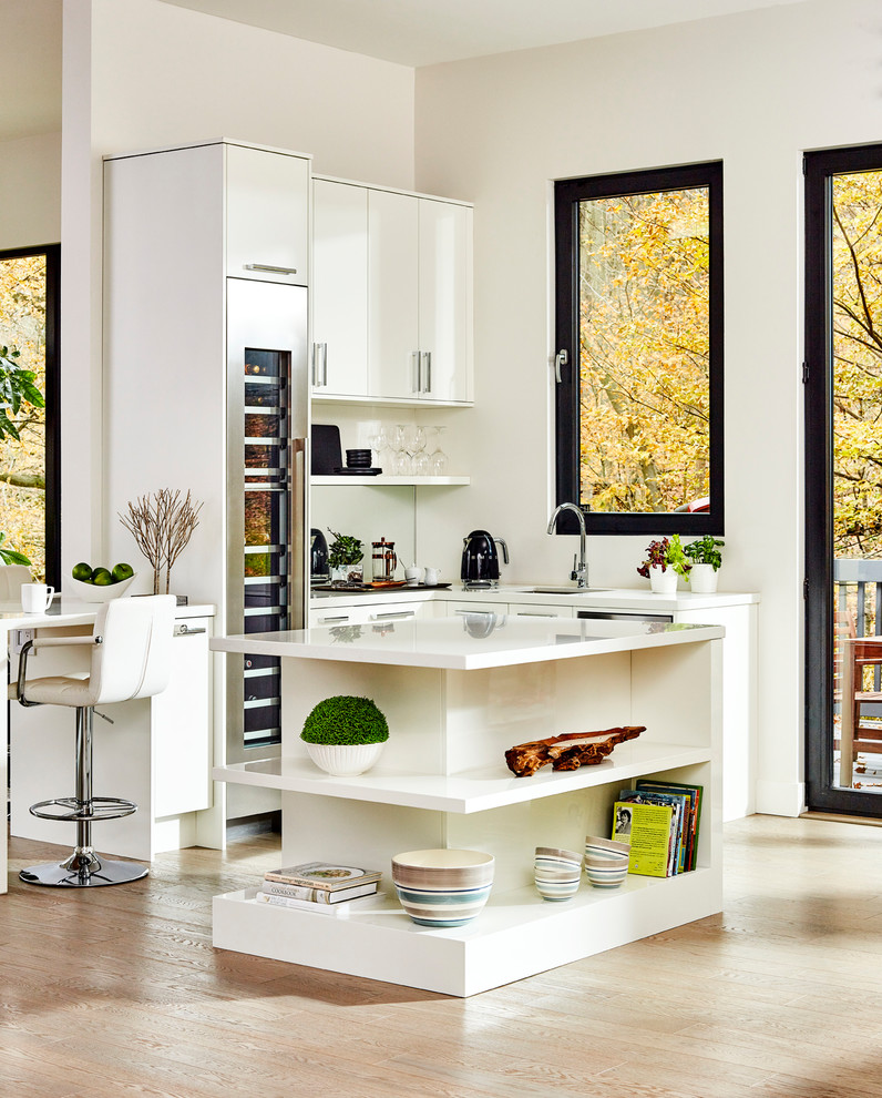 Exempel på ett stort modernt vit vitt l-kök, med en undermonterad diskho, släta luckor, vita skåp, spegel som stänkskydd, rostfria vitvaror, ljust trägolv, en köksö och beiget golv
