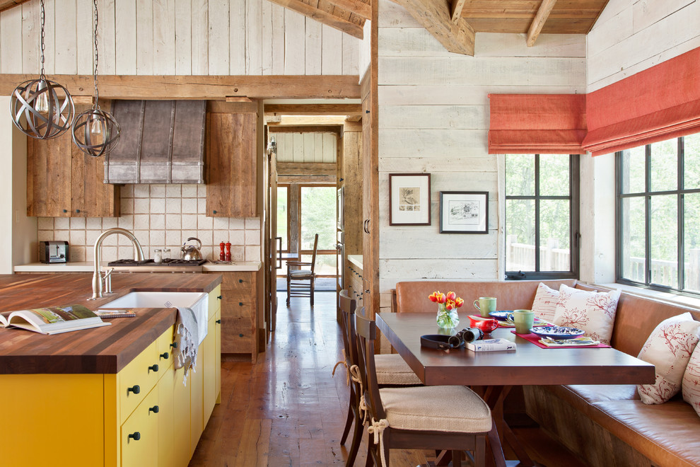 Urige Wohnküche mit Landhausspüle, hellbraunen Holzschränken, Arbeitsplatte aus Holz, Küchenrückwand in Beige, braunem Holzboden, Kücheninsel und orangem Boden in Sonstige