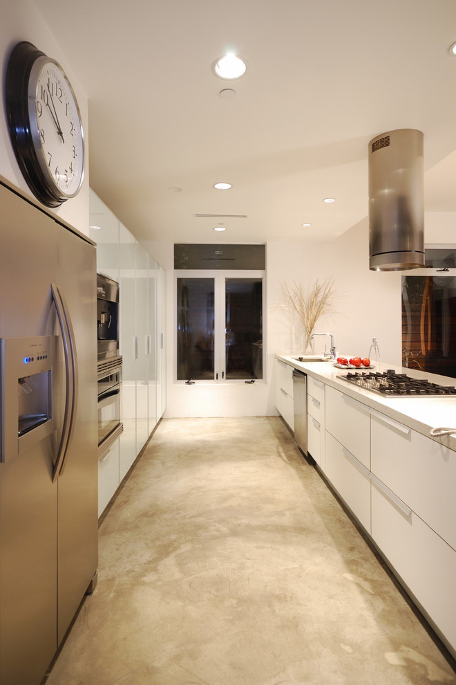 This is an example of a modern galley open plan kitchen in Los Angeles with stainless steel appliances, a submerged sink, flat-panel cabinets, white cabinets, engineered stone countertops and concrete flooring.