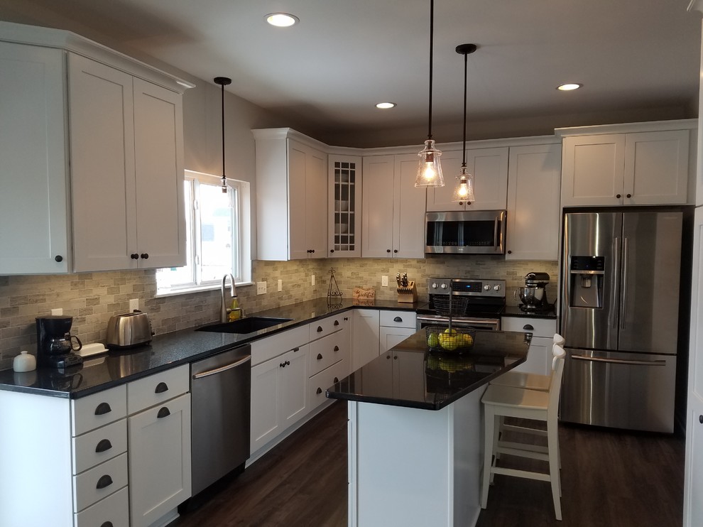 Kitchen - mid-sized traditional vinyl floor kitchen idea in Milwaukee with a double-bowl sink, shaker cabinets, white cabinets, granite countertops, gray backsplash, travertine backsplash, stainless steel appliances and an island