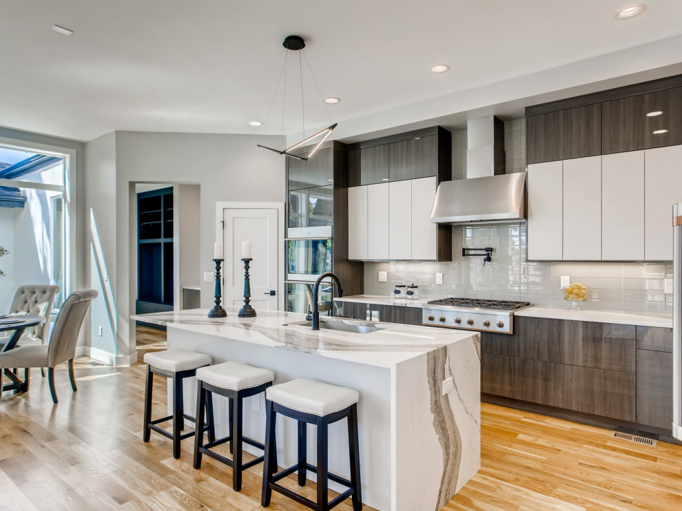 Large contemporary l-shaped kitchen/diner in Denver with a submerged sink, flat-panel cabinets, grey cabinets, grey splashback, ceramic splashback, stainless steel appliances, light hardwood flooring, an island, brown floors and white worktops.