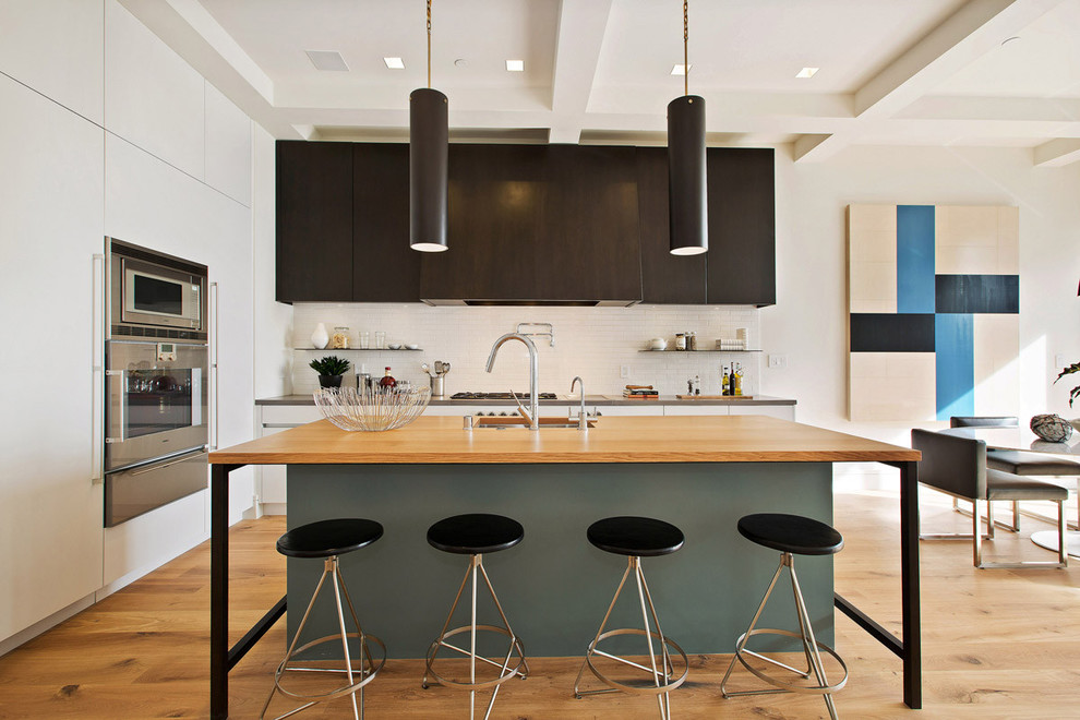 Photo of a contemporary kitchen/diner in San Francisco with flat-panel cabinets, white splashback, stainless steel appliances, light hardwood flooring and an island.