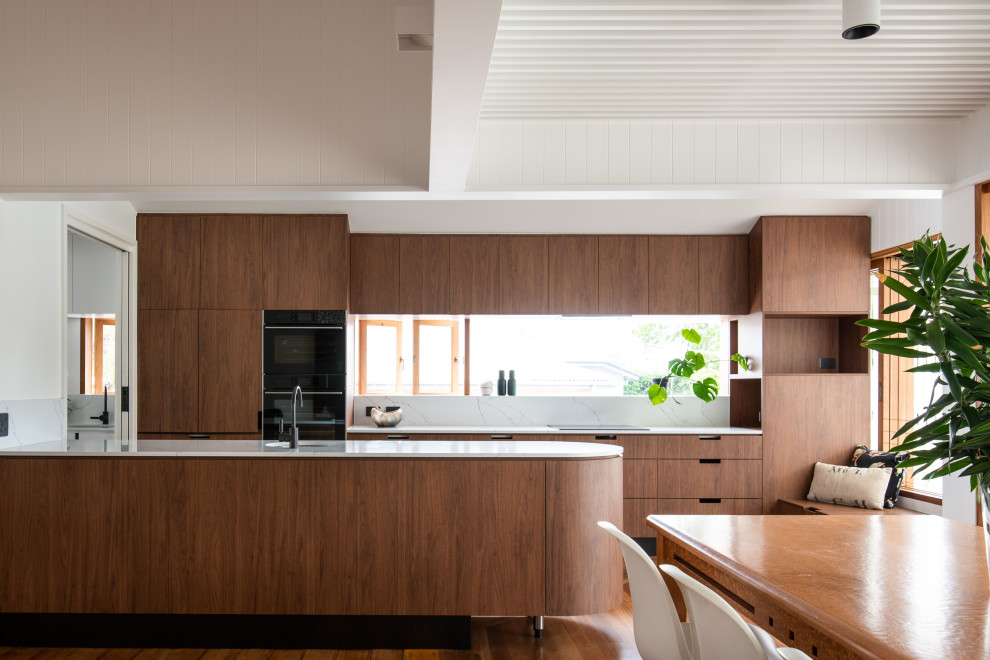 Photo of a medium sized contemporary galley kitchen/diner in Brisbane with engineered stone countertops, an island, white worktops, a submerged sink, flat-panel cabinets, medium wood cabinets, window splashback, black appliances, medium hardwood flooring and brown floors.