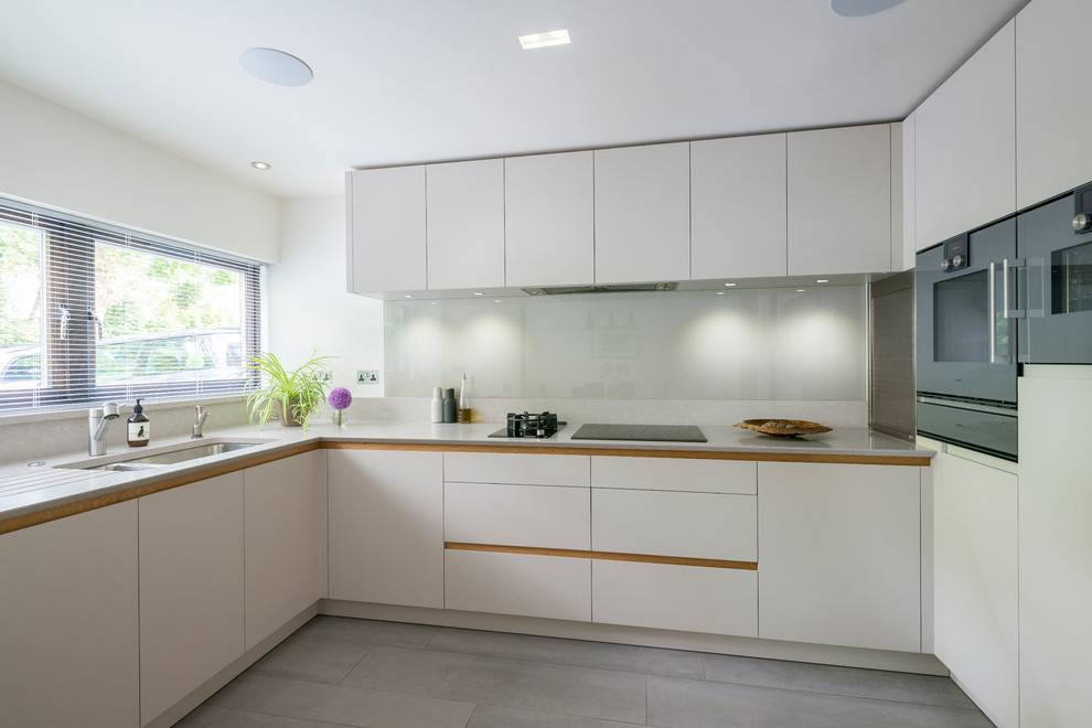 Moderne Wohnküche ohne Insel in L-Form mit flächenbündigen Schrankfronten, weißen Schränken und braunem Holzboden in London