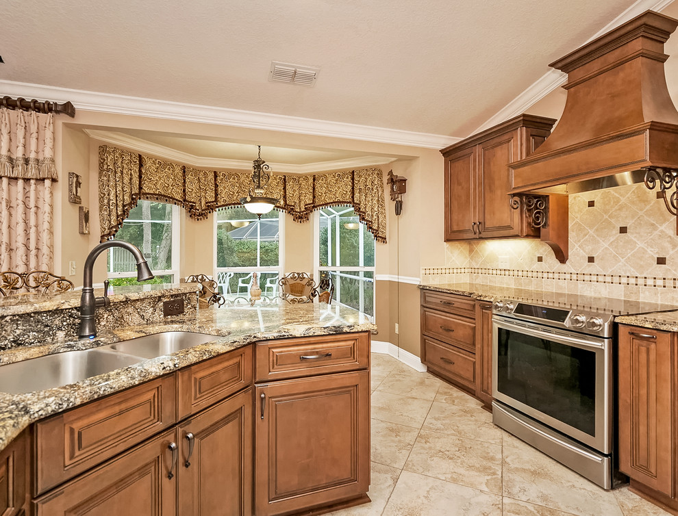 Example of a tuscan u-shaped porcelain tile and beige floor kitchen design in Jacksonville with a drop-in sink, raised-panel cabinets, medium tone wood cabinets, granite countertops, beige backsplash, stone tile backsplash, stainless steel appliances and multicolored countertops